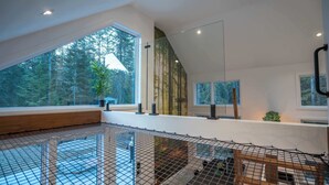 A spacious room with a high ceiling, large windows, and a view of trees.
