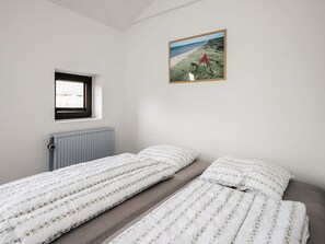 Une chambre avec deux lits simples, une fenêtre, un radiateur et un tableau encadré au mur.