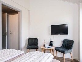 Una habitación de hotel con una cama, dos sillas, una mesita, un televisor y una puerta.