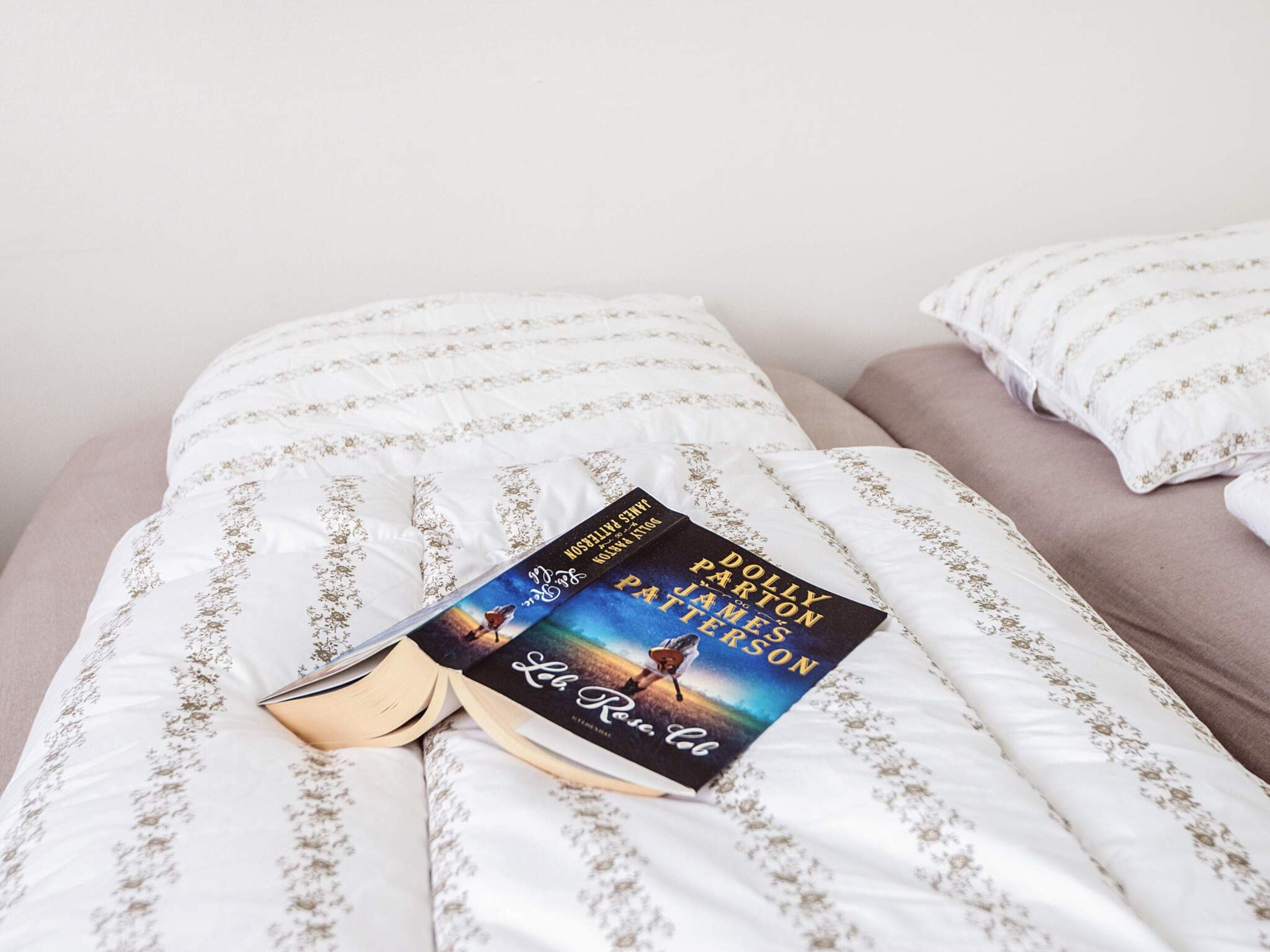 Un libro con el título 'La Reine Rouge' sobre una cama con ropa blanca y una almohada.