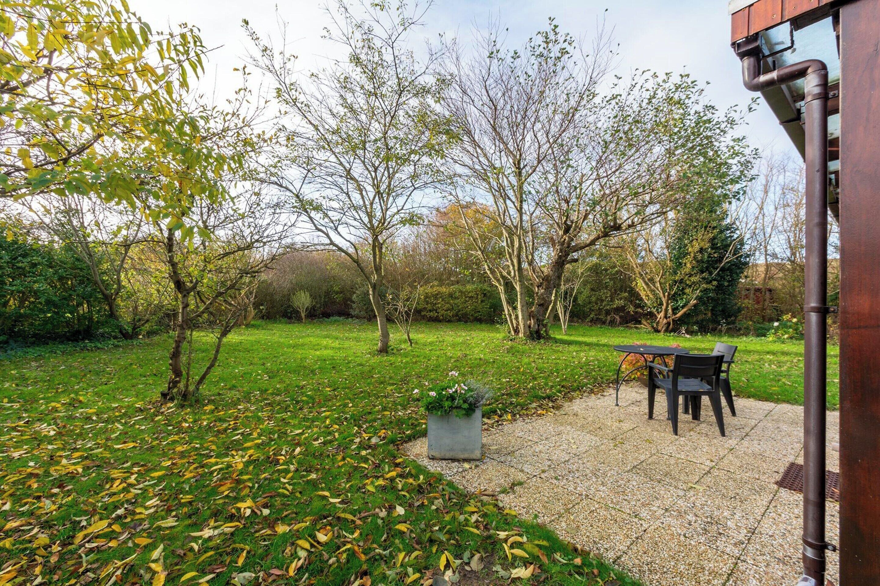 A garden patio with a table and chairs, surrounded by trees and a grassy area.