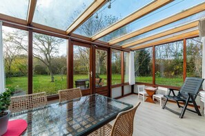 A conservatory with a glass table and wicker chairs, surrounded by wooden frames and large windows. - Orchis4 Bungalow Near Dunes in Julianadorp (Julianadorp)
