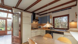 A modern kitchen with wooden beams, a dining table with chairs, and a large window. - Orchis4 Bungalow Near Dunes in Julianadorp (Julianadorp)