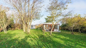 A modern house with a glass facade, surrounded by a well-maintained lawn and trees. - Orchis4 Bungalow Near Dunes in Julianadorp (Julianadorp)
