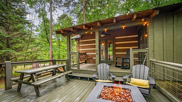 A wooden deck with picnic tables and chairs, a fire pit, and a covered seating area with a ceiling fan.