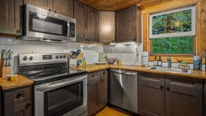 A modern kitchen with stainless steel appliances, wooden cabinets, and a window with a view of greenery.