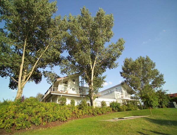 A two-story house with a balcony, surrounded by lush greenery and trees. - Elegant Eingerichtete Ferienwohnung (Mirow)