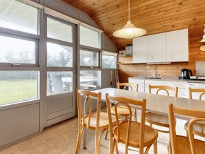 Ett modernt kök med stora fönster, träpanel i taket och en matplats med trästolar.
