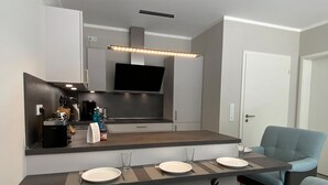 A modern kitchen with a built-in TV, a dark countertop, and a light blue chair.