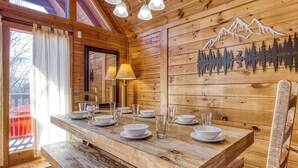 A wooden dining table set with white plates and glasses, a bench, and a wall with a mountain and forest cutout design. - ABOVE THE CLOUDS! 4 Bedroom in the Smokies! (Gatlinburg)