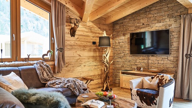 A cozy living room with a stone wall, wooden ceiling beams, a large TV, and a fireplace. - Chalet in Leutasch Near Ski Trails (Leutasch)
