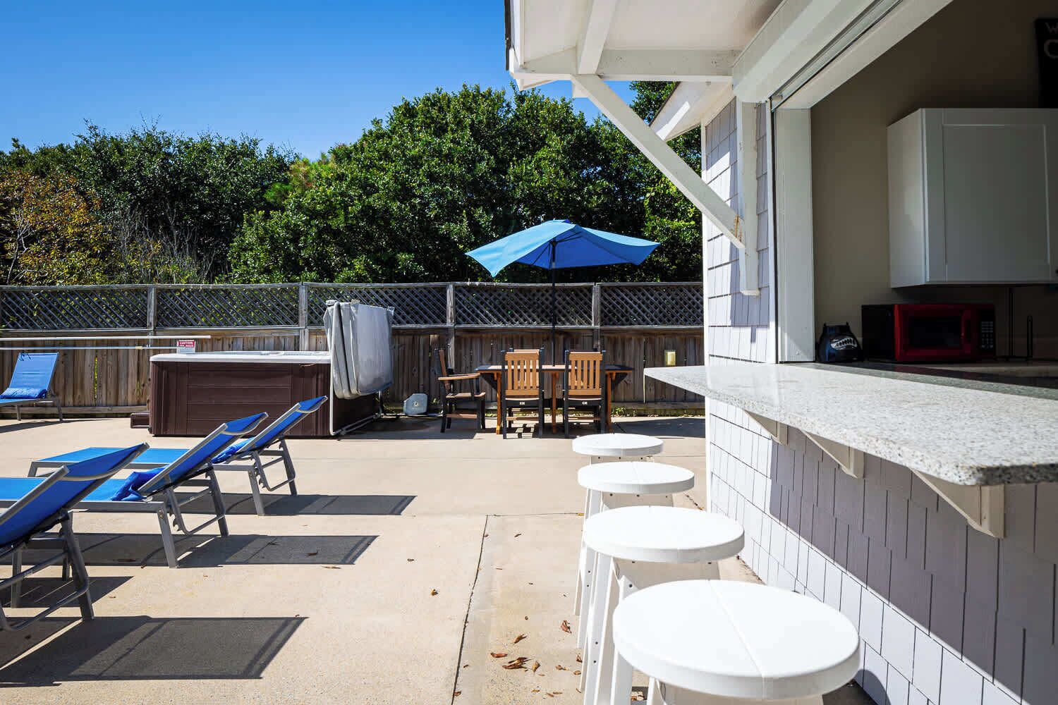 Un espace patio aménagé avec des chaises longues, un barbecue et un coin salon abrité.