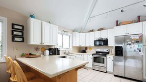 A modern kitchen with white cabinets, a stainless steel refrigerator, a built-in oven, and a large island with bar stools.