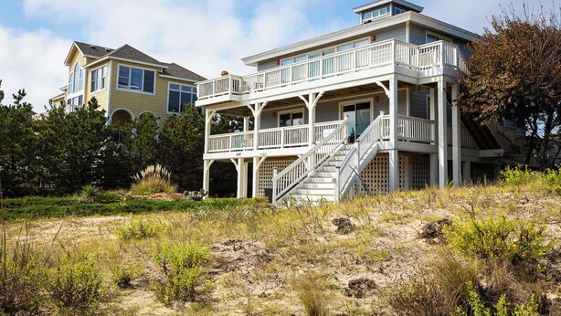 A coastal house with a balcony, a staircase, and a view of the beach.