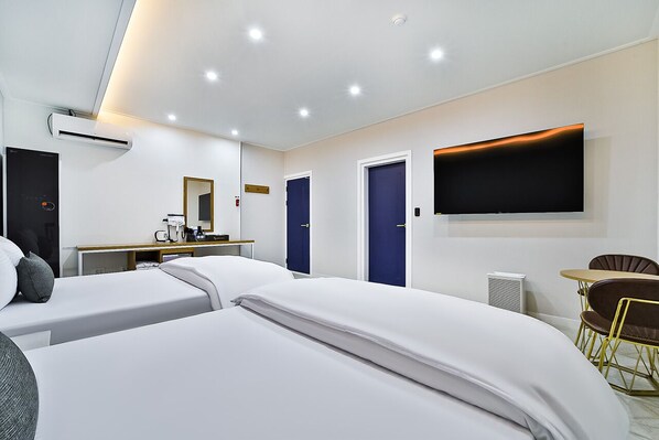 A hotel room with two beds, a desk with a chair, a TV mounted on the wall, and a small dining table with chairs. - Gimcheon Sweet Hotel (Gimcheon)