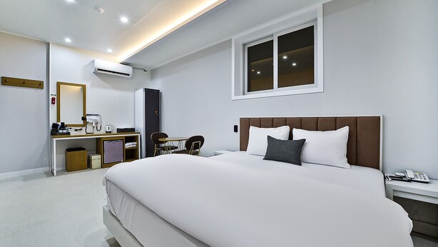 Une chambre d’hôtel moderne avec un grand lit, un bureau avec une chaise, une petite table et une fenêtre.