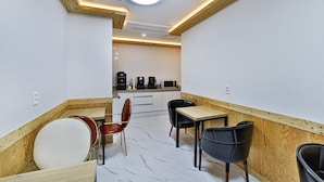 Une cuisine moderne avec des meubles blancs et un plan de travail en bois. On y trouve deux chaises noires et une chaise rouge disposées autour d’une petite table.