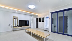 Une pièce moderne et bien éclairée, avec un banc en bois, un téléviseur à écran plat, un réfrigérateur et une porte coulissante à cadre bleu.