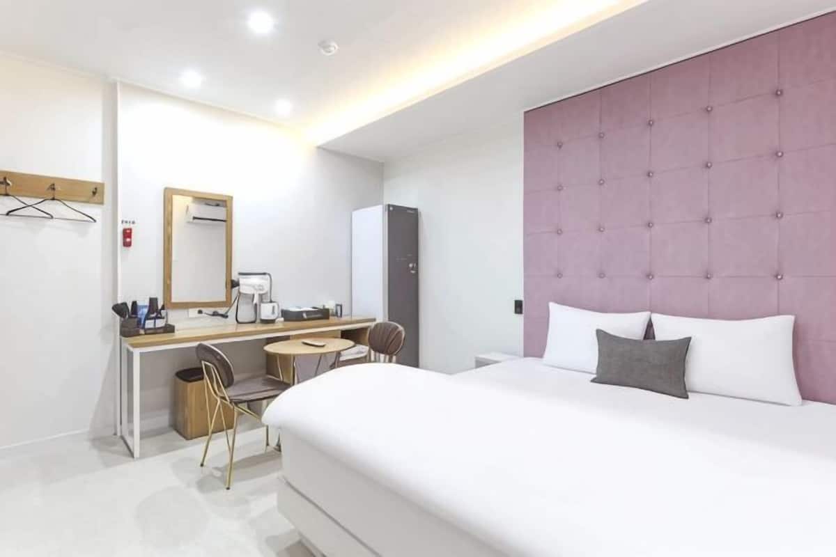 A hotel room with a bed, a desk, a chair, a mirror, and a wardrobe.