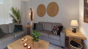 Un soggiorno moderno con un divano grigio, un tavolino in legno con candele, una lampada e un pannello decorativo intrecciato.