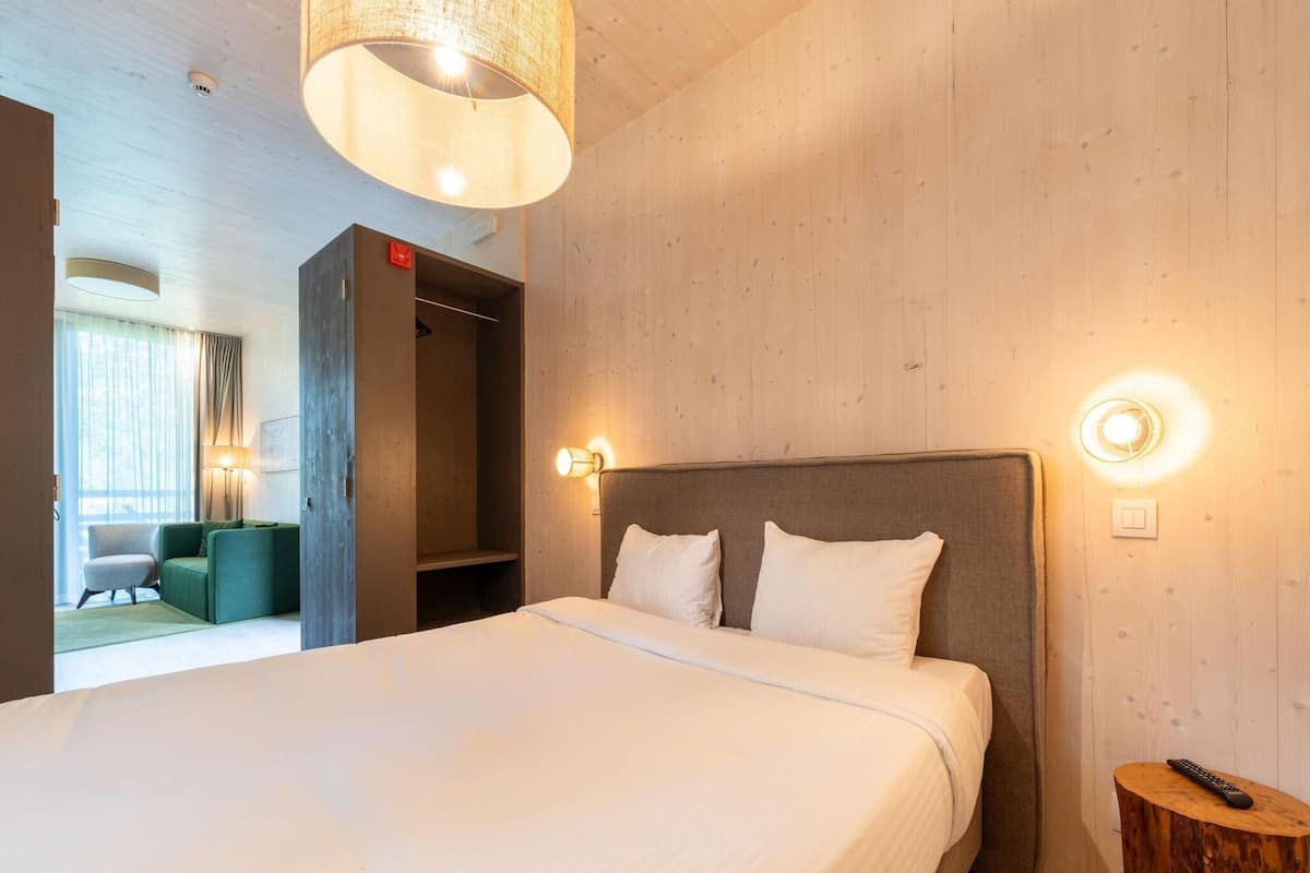 A hotel room with a large bed, a wooden headboard, a bedside table, and a lamp.
