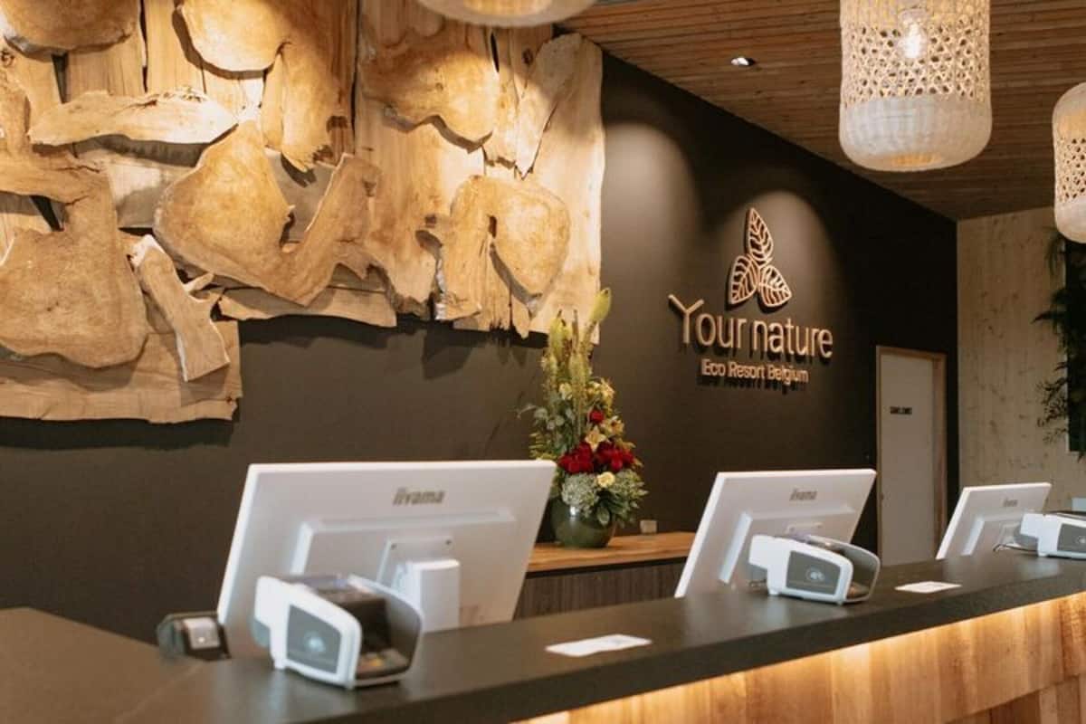 A reception desk with a wooden wall backdrop and a logo that reads "Your nature ECO Resort Belgium."