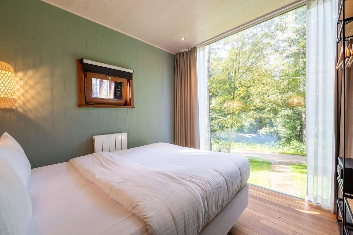 A bedroom with a large bed, a window with curtains, a radiator, and a wall-mounted light fixture.
