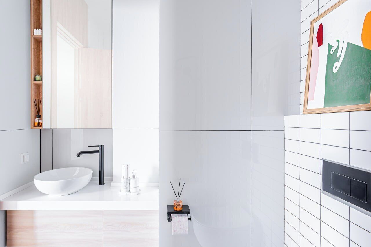 Un baño moderno con lavamanos blanco, grifo negro y un estante pequeño con una botella y difusor de cañas.