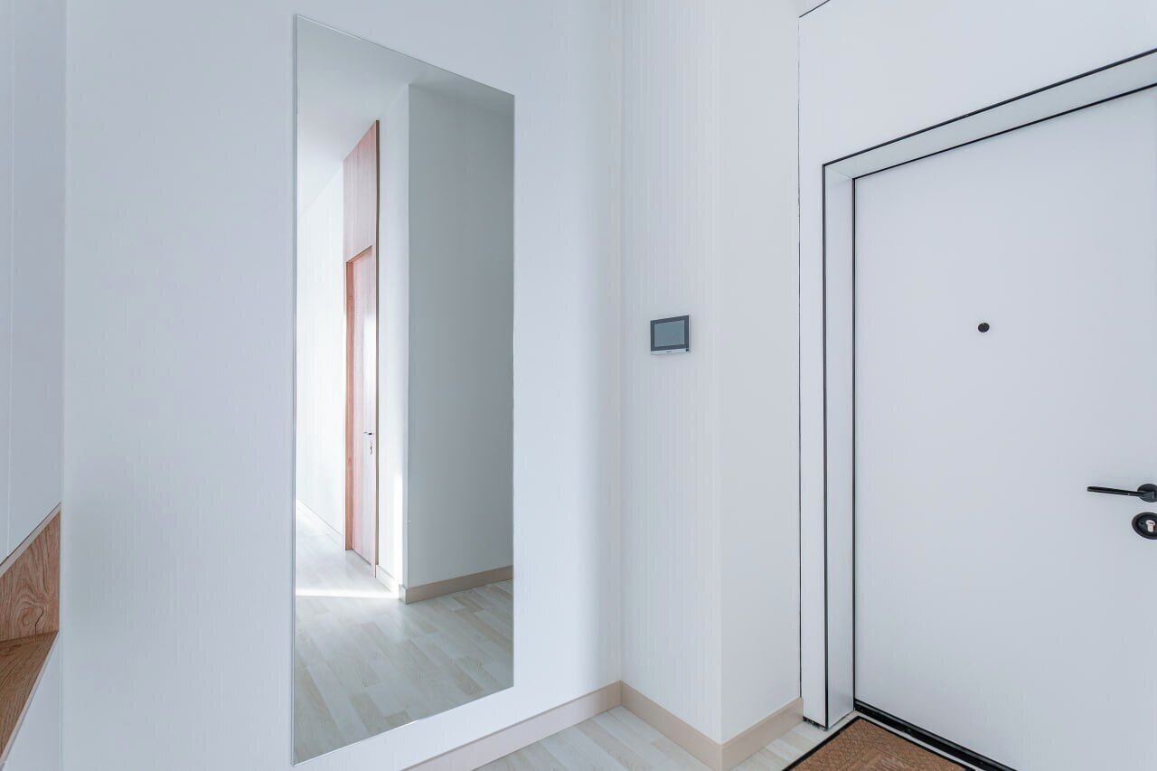 Un pasillo con una puerta blanca, una pantalla pequeña y suelo de madera.