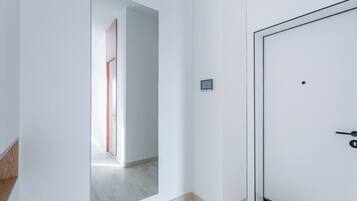 Un pasillo con una puerta blanca, una pantalla pequeña y suelo de madera.