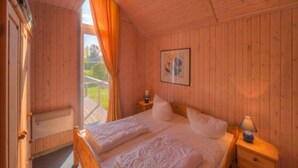 Une chambre à coucher aux murs lambrissés, avec un lit, une table de chevet, une lampe et une fenêtre avec des rideaux.