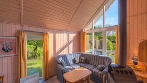 Une pièce chaleureuse avec un plafond en bois, une grande fenêtre, un canapé à rayures, une petite table et un poêle à bois.