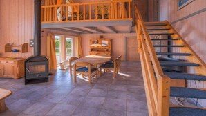 Un intérieur de chalet chaleureux avec un coin repas, un escalier en bois et une cheminée.