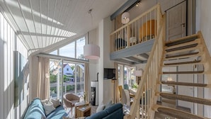 A spacious living area with a blue sofa, wooden staircase, and large windows offering a view of the outside. - Ferienhaus im Skandinavischen Stil (Rechlin)