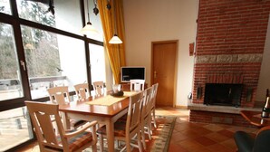 Zona pranzo con tavolo e sedie in legno, camino e vista attraverso ampie finestre.