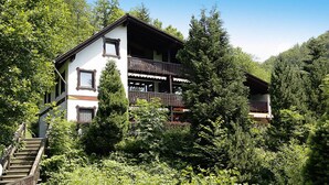 Un chalet a due piani con un balcone, immerso in una fitta foresta.