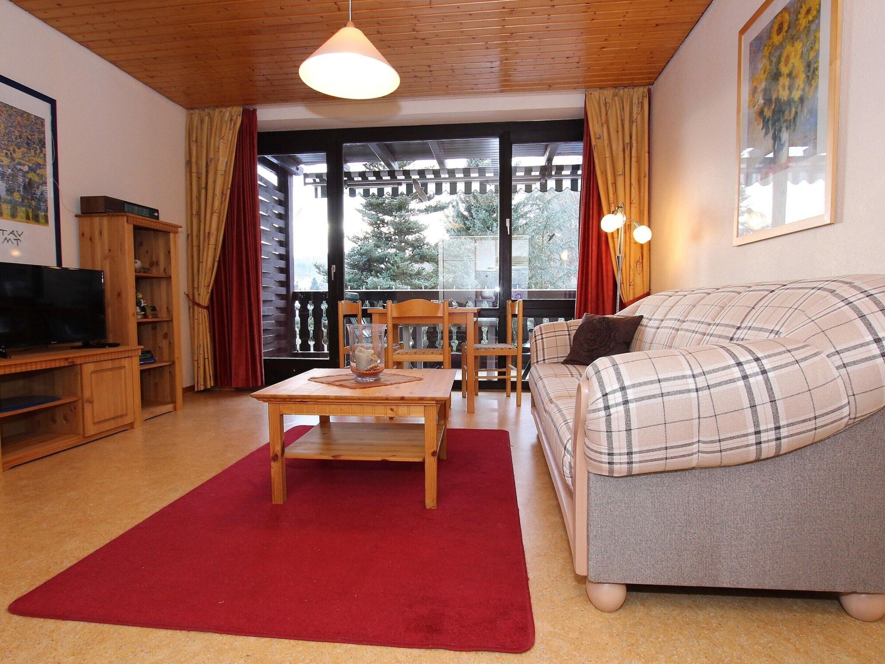 A cozy living room with a sofa, a television, a wooden table, and a red rug.
