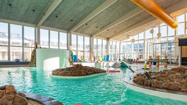 Ein Hallenbad mit klarem Wasser, Felsformationen und farbenfrohen, herzförmigen Kacheln.