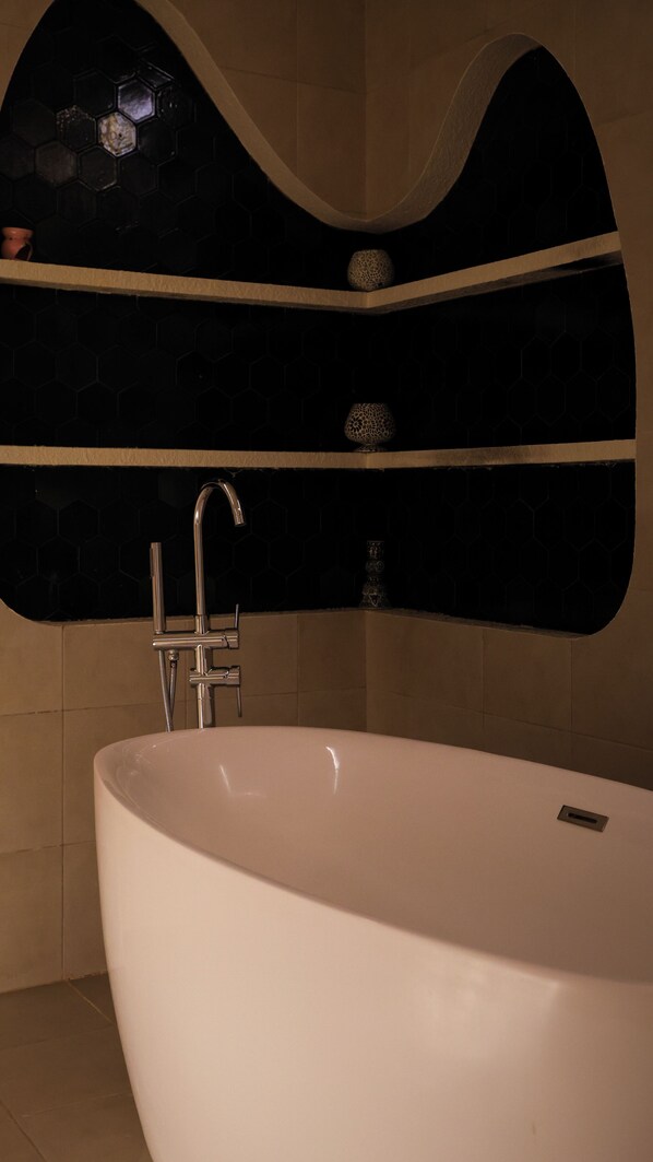 A modern bathroom with a freestanding bathtub, a curved wall with hexagonal tiles, and a shower area with a glass enclosure. - AlIskan Al Tullabi - Female Only (Seeb)