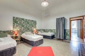 A hotel room with two beds, a red mat, a wall with a tropical wallpaper, an air conditioning unit, and a door leading to a hallway. - Faenza 64 in Firenze (Florence)
