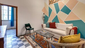 Een woonkamer met een geruite vloer, een bank, een salontafel, een rieten stoel en een vloerkleed met een patroon.