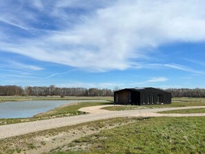 Un bâtiment à l’extérieur sombre, situé près d’une étendue d’eau et d’un chemin de gravier.