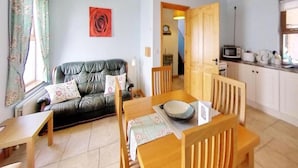 Een woonkamer met een bank, een eettafel met stoelen, een keukenhoek met een magnetron en een trap naar een andere kamer.