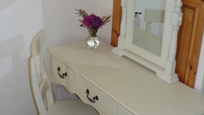 Een witte ladekast met spiegel en een vaas met paarse bloemen.
