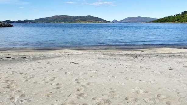 Una spiaggia con acque cristalline, una riva sabbiosa e colline in lontananza.