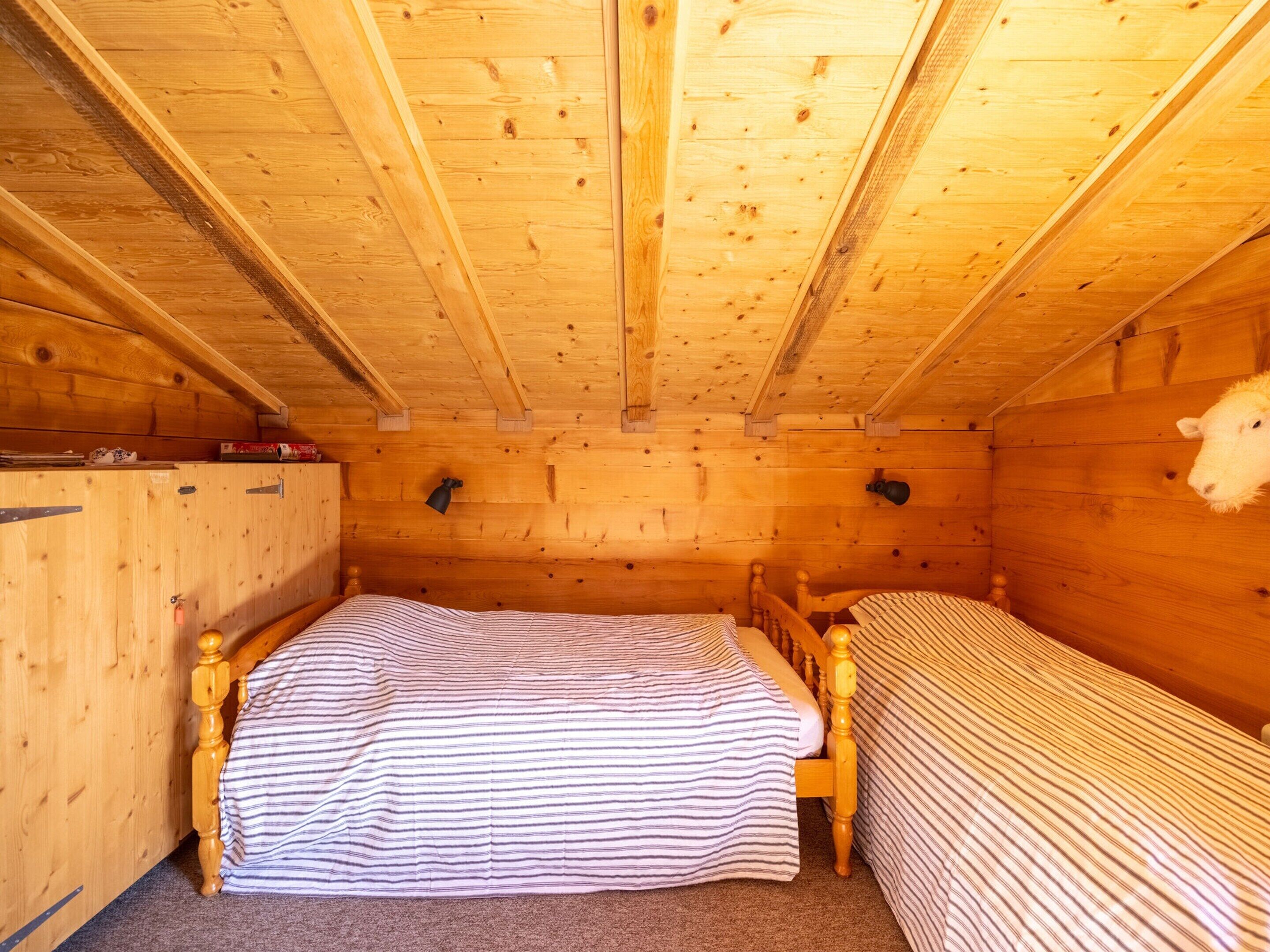 A wooden cabin room with two beds, a wooden ceiling, and a sheep head decoration.