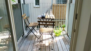 Eine Holzterrasse mit Tisch und zwei Stühlen, einem Laptop, einer Wasserflasche und Kübelpflanzen.