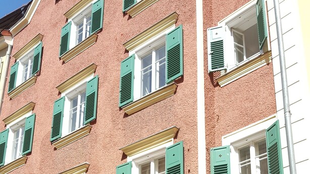 Ein mehrstöckiges Gebäude mit grünen Fensterläden, ein sichtbares Geschäft mit einem Schild für 'Dizzy's by Rick' und eine Uhr auf der rechten Seite.