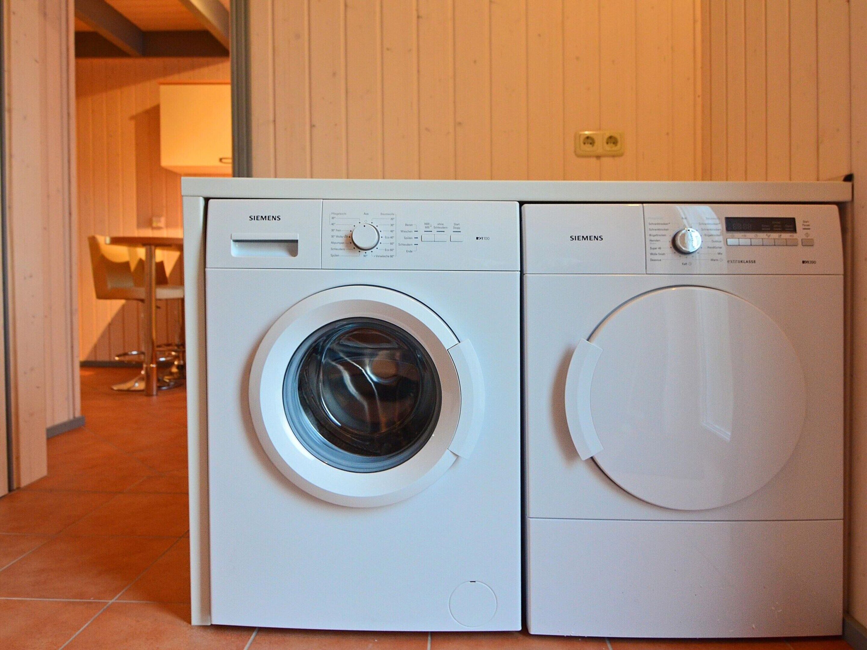 A front-loading washer and dryer side by side in a room with wooden walls and a tiled floor.