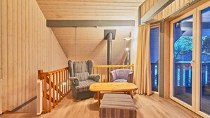 Ein gemütlicher Raum mit Holzwänden und schrägen Decken, ausgestattet mit einem Holztisch, zwei gepolsterten Stühlen, einer Bank und einem großen Fenster mit Aussicht.